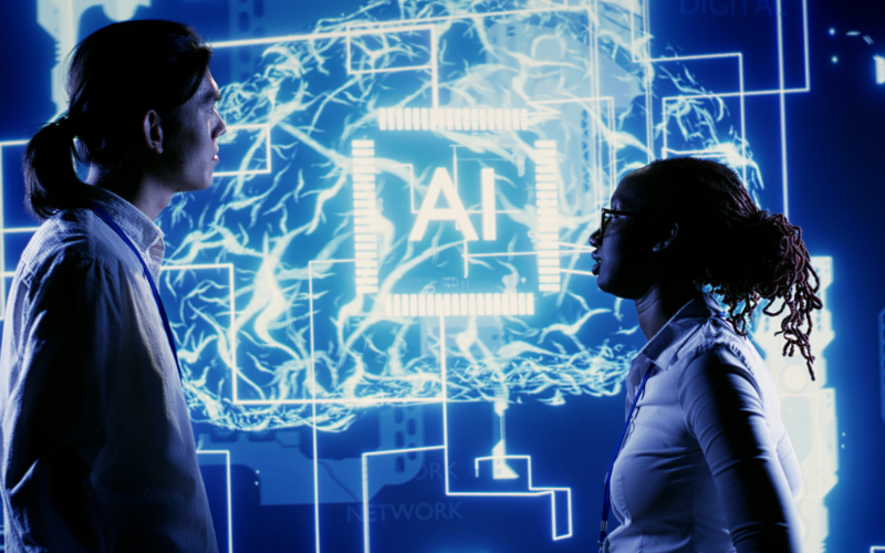 Dos profesionales analizando una interfaz digital con un sistema de Inteligencia Artificial, representando cómo la GenAI impulsa la innovación y automatización en fábricas de software modernas.